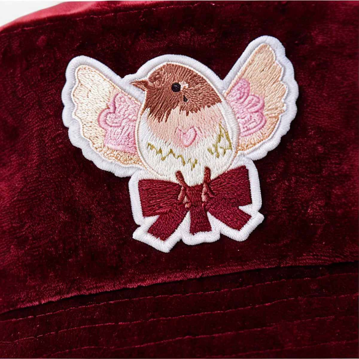 Close up of the embroidered robin and burgundy bow on the velvet bucket hat