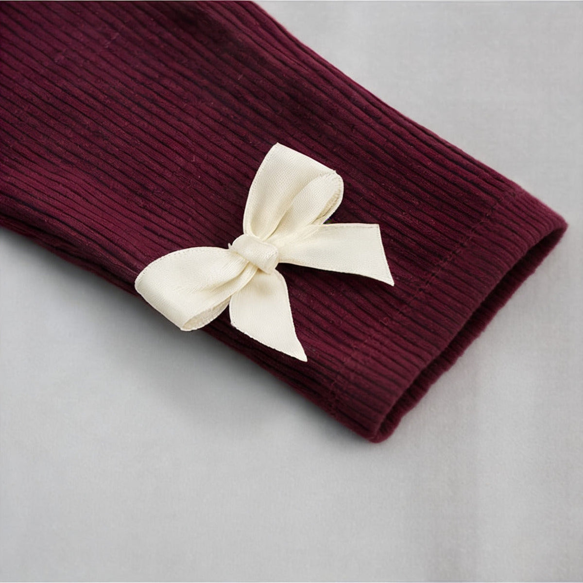 Close up of the cream ribbon bow on the ribbed cuff of the burgundy Robin Soft Borg Set