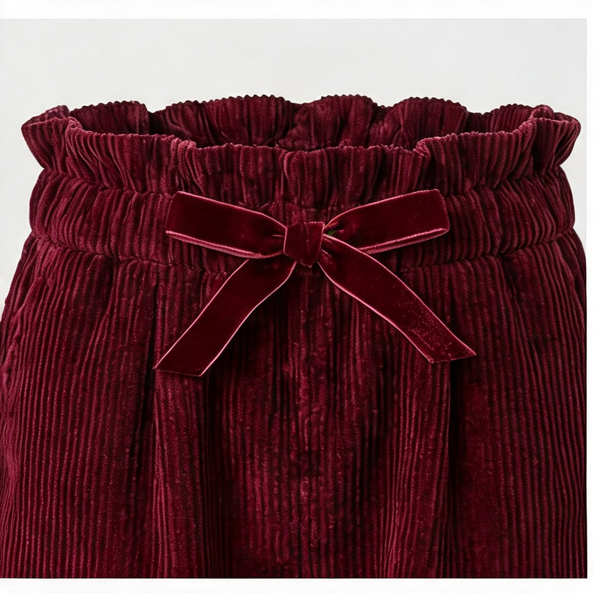 Close-up of the burgundy velvet bow and ruffled paperbag waistband on the Robin Needlecord Trousers